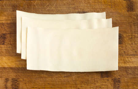 Heap of Uncooked Lasagna Sheets or Dry Italian Pasta on Old Wooden Cutting Boardの写真素材
