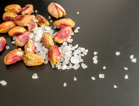 Heap of Inshell Pistachios and Peeled Pistachios with Large Salt Crystals on Black Background