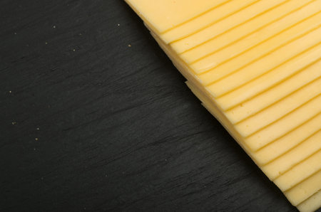 Sliced Cheese Over Black Stone Background with Space for Text Top View