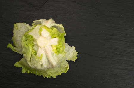 Round Iceberg Lettuce on Black Stone Background. Green Salad Head with Place for Textの写真素材