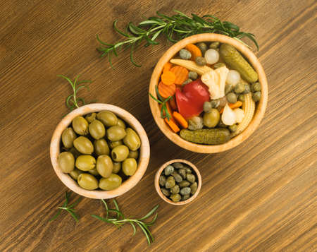 Mixed Pickles in Wood Bowls Top View. Marinated Cucumber, Carrot, Perl Onion, Baby Corn, Paprika or Red Pepper, Cauliflower, Olives and Capersの写真素材