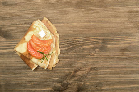 Crepes with Raw Sliced Salmon Fillet. Thick Pieces of Red Trout with Pancakes on Dark Wooden Backgroundの写真素材
