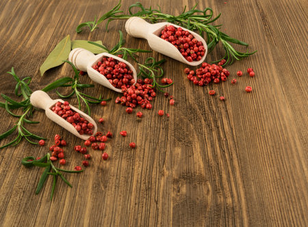 Pink Pepper or Red Pepper Corns on Wooden Background. Schinus Dry Seeds with Fresh Rosemary on Wood Rustic Tabletopの写真素材