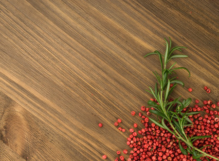 Pink Pepper or Red Pepper Corns on Wooden Background. Schinus Dry Seeds with Fresh Rosemary on Wood Rustic Tabletopの写真素材