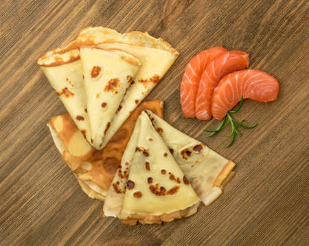 Crepes with Raw Sliced Salmon Fillet. Thick Pieces of Red Trout with Pancakes on Dark Wooden Backgroundの写真素材