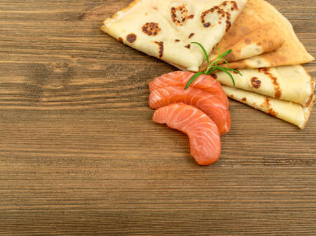 Crepes with Raw Sliced Salmon Fillet. Thick Pieces of Red Trout with Pancakes on Dark Wooden Backgroundの写真素材