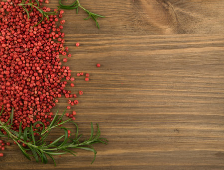 Pink Pepper or Red Pepper Corns on Wooden Background. Schinus Dry Seeds with Fresh Rosemary on Wood...