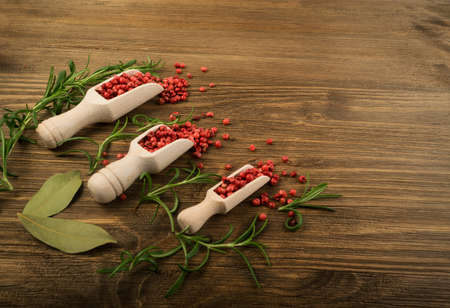 Pink Pepper or Red Pepper Corns on Wooden Background. Schinus Dry Seeds with Fresh Rosemary on Wood Rustic Tabletopの写真素材