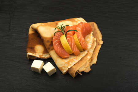 Crepes with Raw Sliced Salmon Fillet. Thick Pieces of Red Trout with Pancakes on Black Stone Backgroundの写真素材