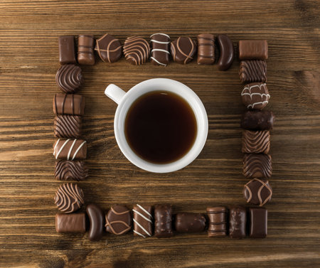 Mix of Chocolate Sweets on Natural Wooden Table with White Coffee Cup. Square Chocolates Frame Top...