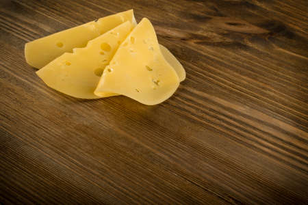 Thin Slices of Swiss Cheese on Wooden Background Top View and Flat Lay. Natural Rustic Backdrop with Place for Textの写真素材