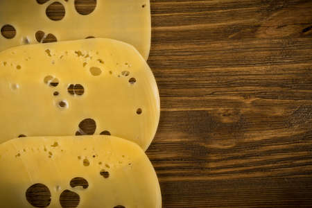 Thin Slices of Swiss Cheese on Wooden Background Top View and Flat Lay. Natural Rustic Backdrop with Place for Textの写真素材