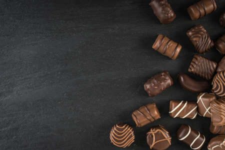 Beautiful Creative Chocolate Sweets on Natural Black Stone Background. Scattered Chocolates Top View and Flat Lay with Place for Textの写真素材