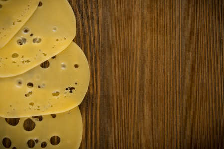 Thin Slices of Swiss Cheese on Wooden Background Top View and Flat Lay. Natural Rustic Backdrop with Place for Textの写真素材