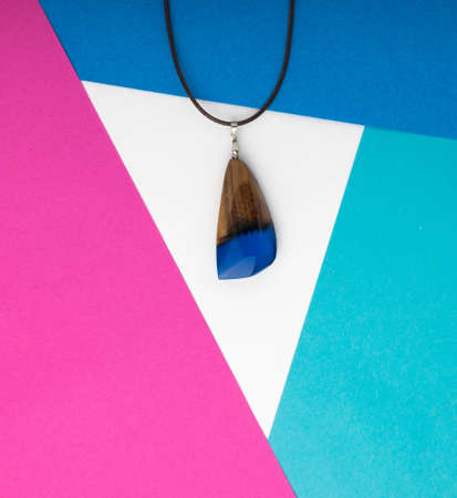 Hand Made Blue Wood Pendant on Abstract Multicolored Geometric Background. Author Creative Bijouterie Made of Epoxy Resin and Woodの写真素材