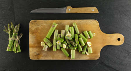 Chopped Raw Garden Asparagus with Garlic ready for Frying Top View. Fresh Green Spring Vegetables on Wooden Background.の写真素材