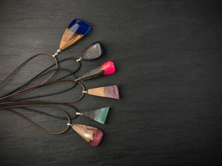 Different Pendants of Pink, Blue and Green Color on Black Stone Background. Bijouterie Made of Epoxy Resin and Wood Top Viewの写真素材