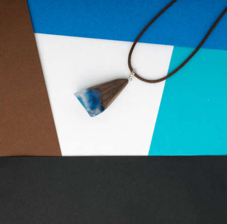 Hand Made Blue Wood Pendant on Abstract Multicolored Geometric Background. Author Creative Bijouterie Made of Epoxy Resin and Woodの写真素材