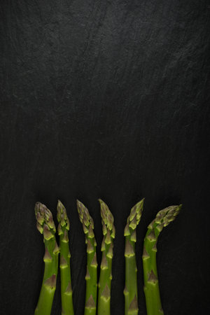 Raw Garden Asparagus Top View. Fresh Green Spring Vegetables on Black Stone Background with Space for Text.の写真素材
