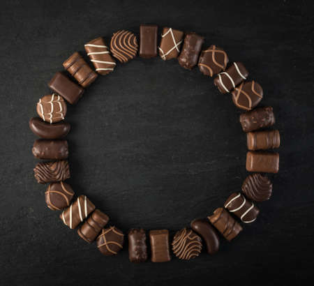 Beautiful Creative Chocolate Sweets on Natural Black Stone Background. Mix of Chocolates in Round Frame Shape Top View and Flat Lay with Place for Textの写真素材