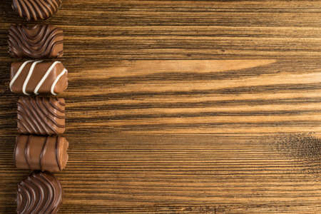 Beautiful Creative Chocolate Sweets on Natural Wooden Table Background. Line of Chocolates Top View with Place for Textの写真素材