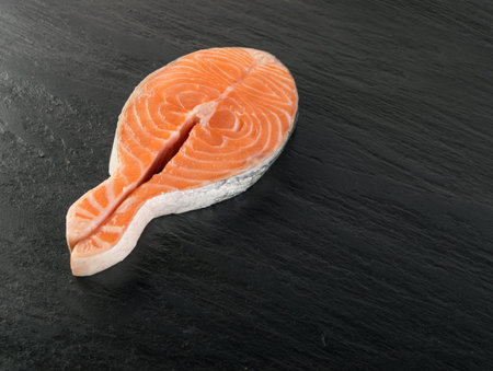 Slice of Raw Salmon Steak on Natural Black Background. Thick Piece of Fresh Red Fish or Trout Top View with Place for Textの写真素材