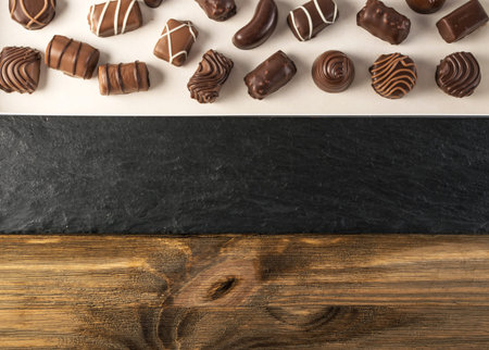 Box with Chocolate Sweets on Natural Black Stone and Wooden Background. Mix of Chocolates Top View...