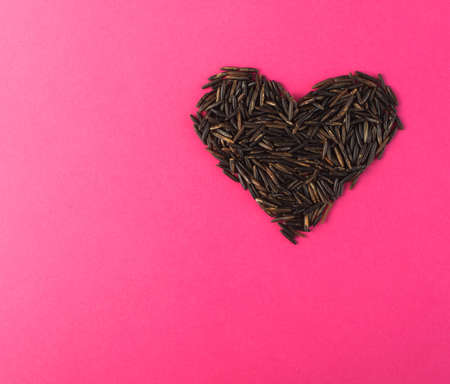 Raw Black Wild Rice Heart on Pink Paper Background Top View. Healthy Dietetic Canada Rice Cereal with Place for Textの写真素材