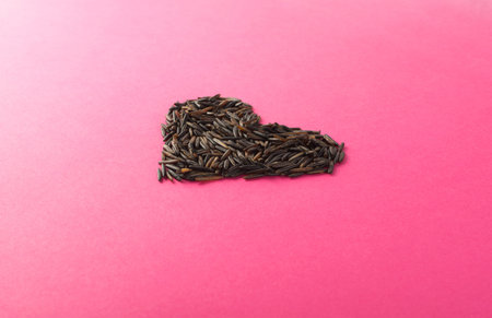 Raw Black Wild Rice Heart on Pink Paper Background.