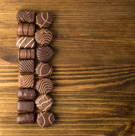 Beautiful Creative Chocolate Sweets on Natural Wooden Table Background. Line of Chocolates Top View with Place for Textの写真素材