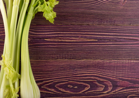 Raw green celery stalks on wood background top view. Fresh organic vegetables on old wooden rustic...