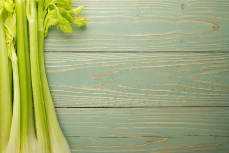 Raw green celery stalks on wood background top view. Fresh organic vegetables on old wooden rustic...