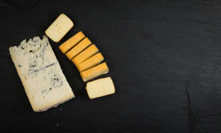 Cheeseboard with Sliced Limburger, Herve Cheese or Reblochon And Blue Gorgonzola, Roquefort or Stilton. Cheese Course with Mix of Yellow and Blue Cheeses Top View on Black Stone Plate Backgroundの写真素材