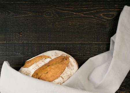 Homemade Freshly Baked Traditional Bread on Dark Wooden Table Top View with Copyspace. Whole Loaf of Rustic Italian Cereal Bread Made of Sourdough Dough with Space for Textの写真素材