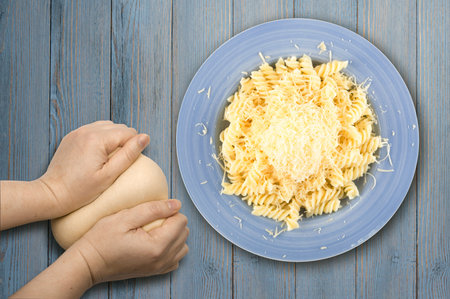 Pile of grated cheese on hot fusilli pasta in blue plate isolated on white background. Homemade...