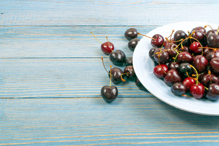 Blue plate of fresh red cherry on old wooden background with copy space for design montage or...