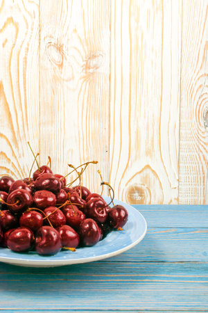 Blue plate of fresh red cherry on old wooden background with copy space for design montage or...