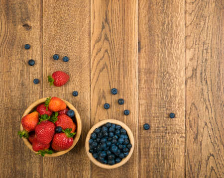 Fresh Beautiful Strawberries and Blueberries on Old Vintage Wooden Background with Copyspace. Dark Wood Table Desk Board Texture with Ripe Forest Berries Top Viewの写真素材