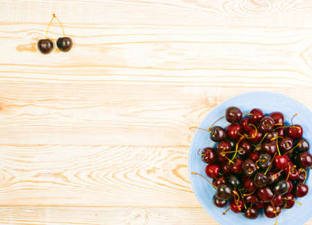 Round plate of fresh ripe cherries on old wooden background for design montage. White wood table desk board with overripe cherries or sweet berries pile top view with copy spaceの写真素材