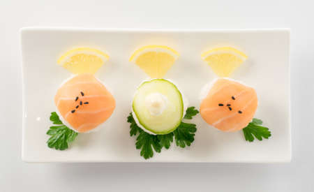 Little Nigiri Sushi or Temarizushi with Salmon and Cucumber on Light Background Top View. Rice Balls with Raw Red Fish on White Plateの写真素材