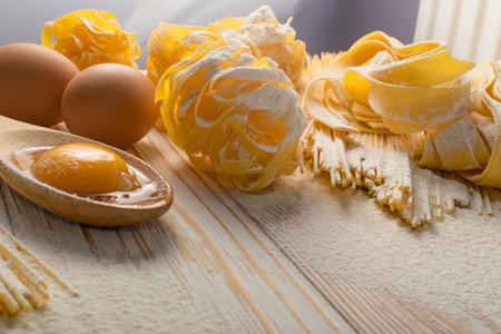 Raw yellow italian pasta pappardelle, fettuccine or tagliatelle close up with eggs. Egg homemade...
