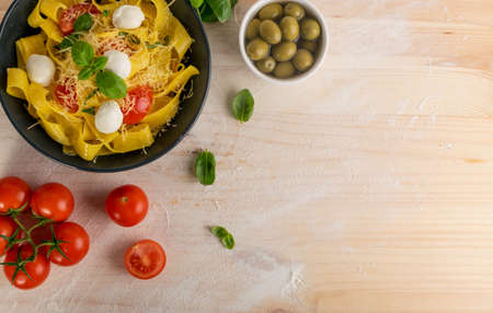 Yellow cooked pasta pappardelle, fettuccine or tagliatelle on black plate top view. Egg homemade ribbon noodles or macaroni with tomatoes, basil and mozzarella balls on wooden rustic backgroundの写真素材