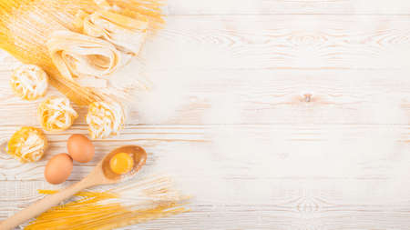 Raw yellow italian pasta pappardelle, fettuccine or tagliatelle close up with eggs. Egg homemade noodles cooking process, long rolled macaroni or uncooked spaghetti against flour background top viewの写真素材