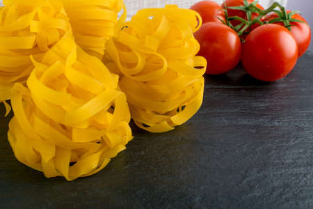 Raw yellow italian pasta fettuccine, fettuccelle or tagliatelle close up. Egg homemade dry ribbon noodles, long rolled macaroni or uncooked spaghetti on black stone backgroundの写真素材