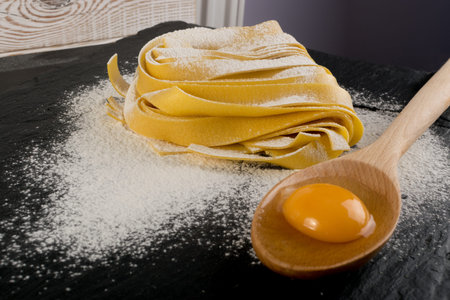Raw yellow italian pasta pappardelle, fettuccine or tagliatelle close up with eggs. Egg homemade...