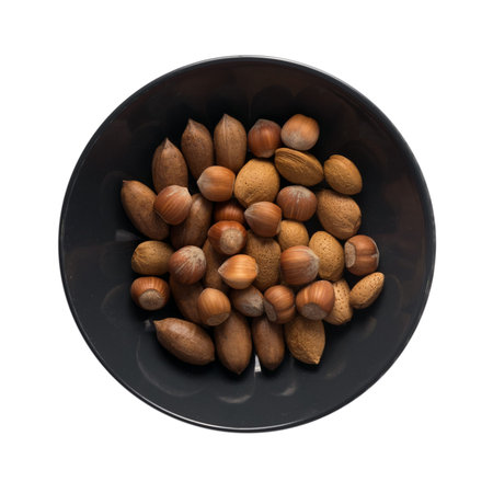 Heap of Macadamia Nuts, Hazelnuts and Almonds in Shell. Nut Mix in Black Bowl Isolated on White Background Top Viewの写真素材