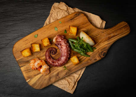Traditional greek grilled seafood on a wooden cut board served with shrimps and vegetables rustic style. Delicious barbecue octopus tentacle with fresh greens top viewの写真素材