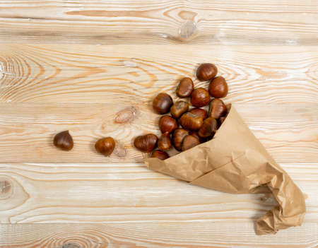 Edible sweet whole chestnuts in paper bag on wood table background top view. Raw healthy delicious chestnut, autumn and christmas european veggie foodの写真素材