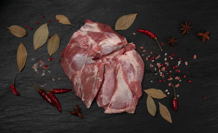 Fresh raw mutton shoulder meat with bone on black stone plate background. Large piece of sheep fillet or filet closeup top viewの写真素材