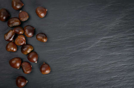 Edible sweet whole chestnuts pattern on black stone background with copy space top view. Set of raw healthy delicious chestnut, autumn and christmas veggie foodの写真素材